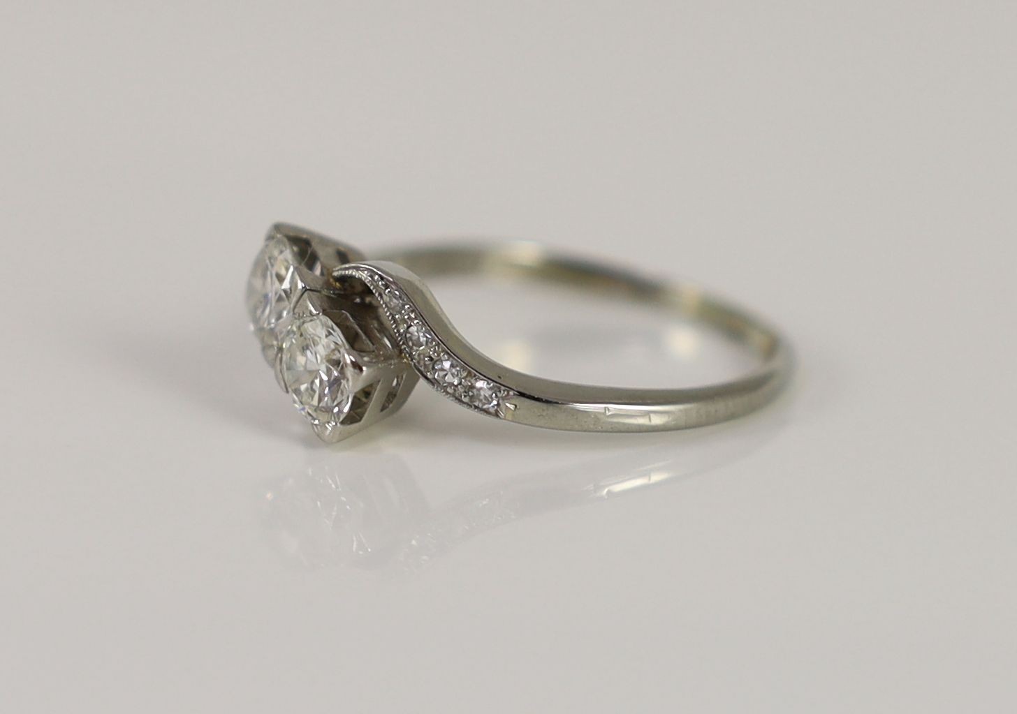 An 18ct gold and two stone diamond crossover ring, with millegrain diamond chip set shoulders